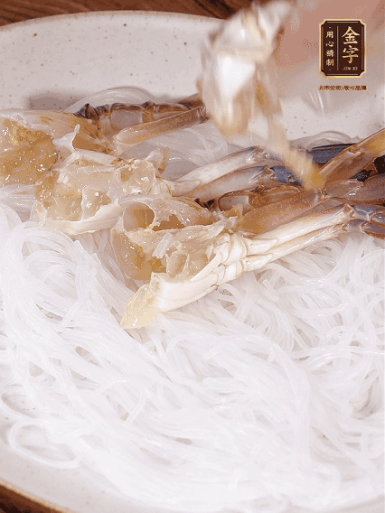 盤底墊上粉絲，擺上梭子蟹、火腿片，撒姜粒，淋上蒸魚豉油、花雕酒調(diào)味腌制15分鐘